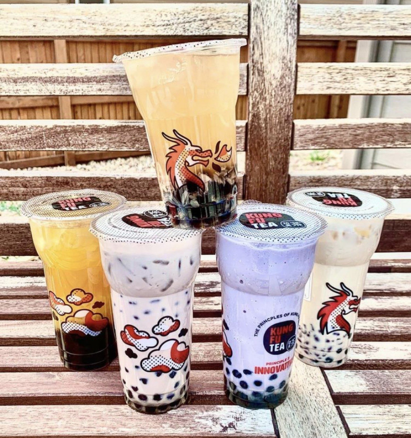 A lineup of five freshly made Kung Fu Tea drinks — milk tea, oolong and fruit tea — on a wooden bench