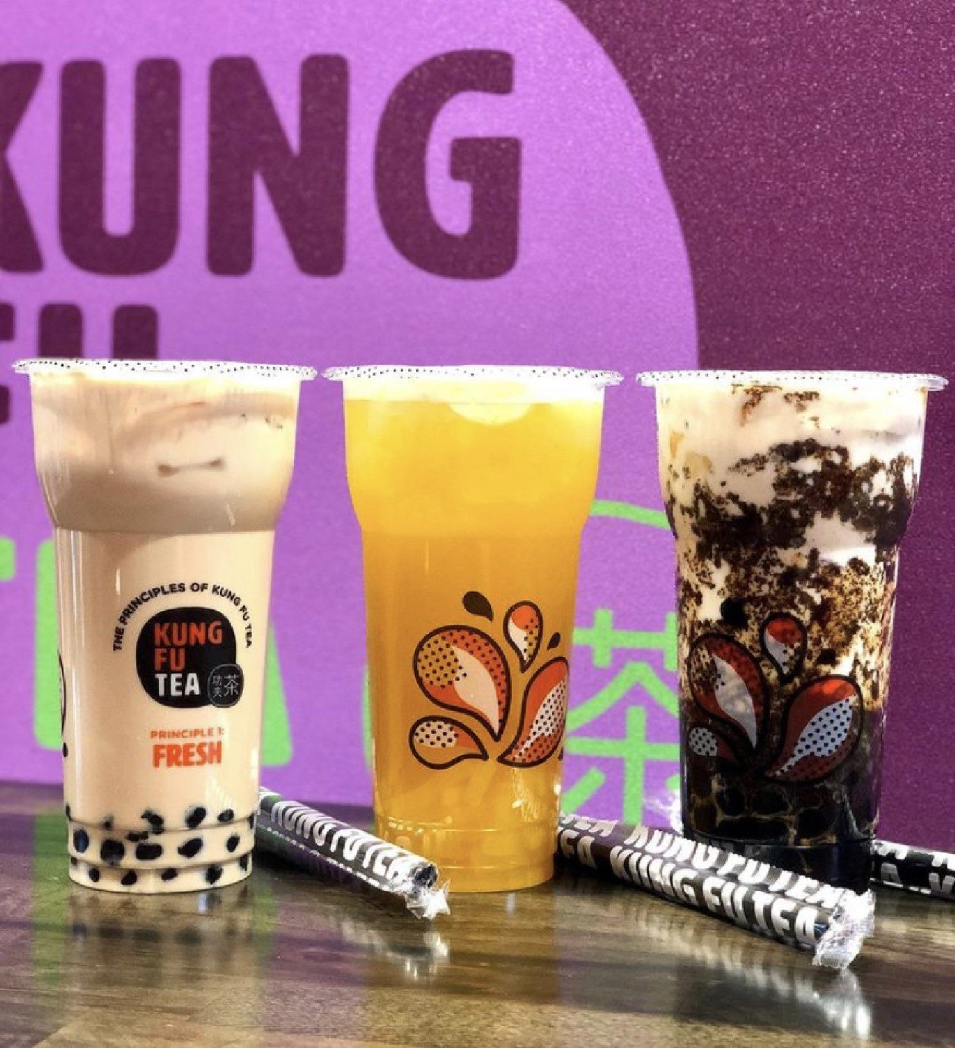 Three Kung Fu Tea drinks in front of a purple Kung Fu Tea wall mural