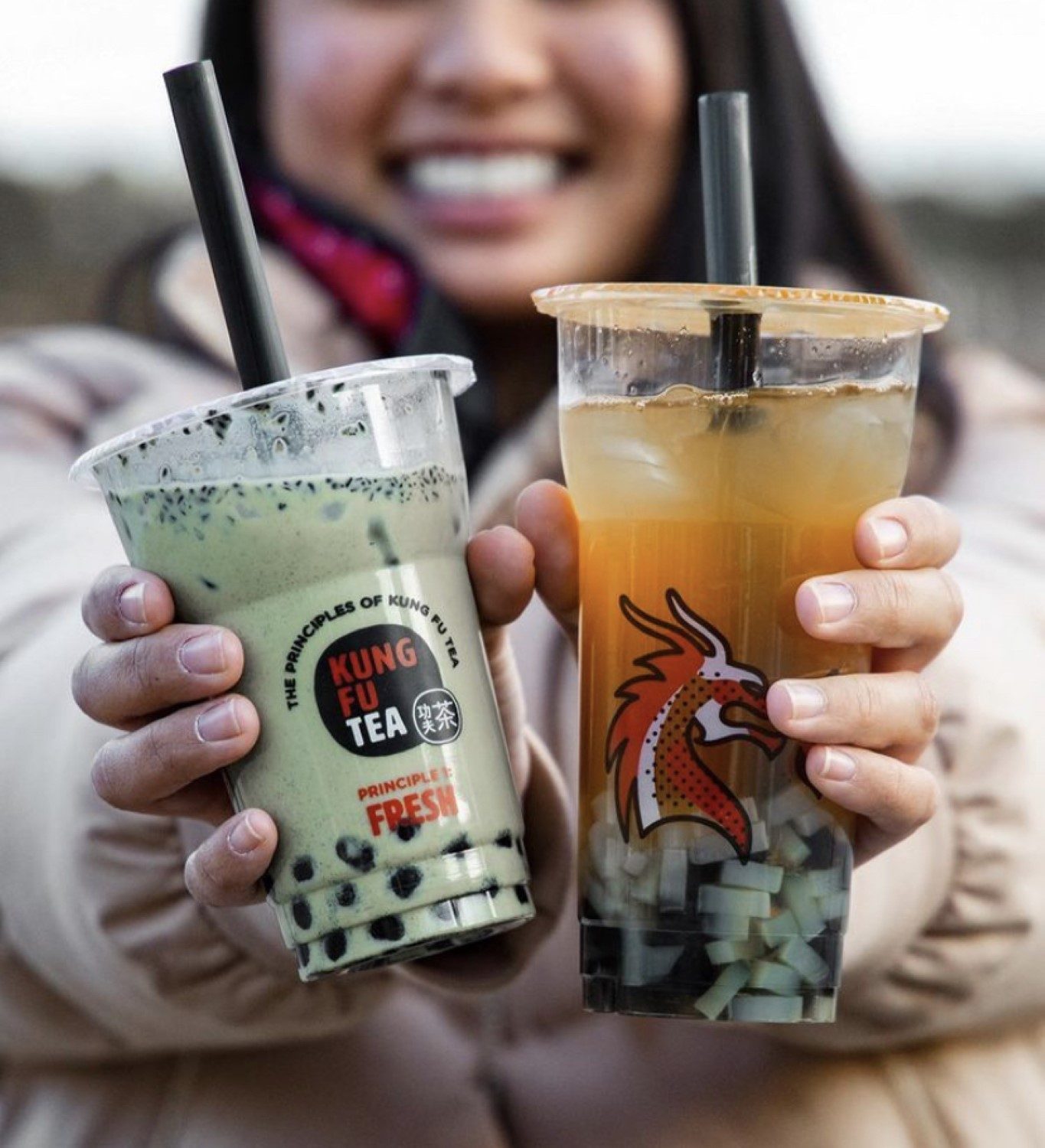 A customer smiling while holding matcha and mango green tea drinks from Kung Fu Tea