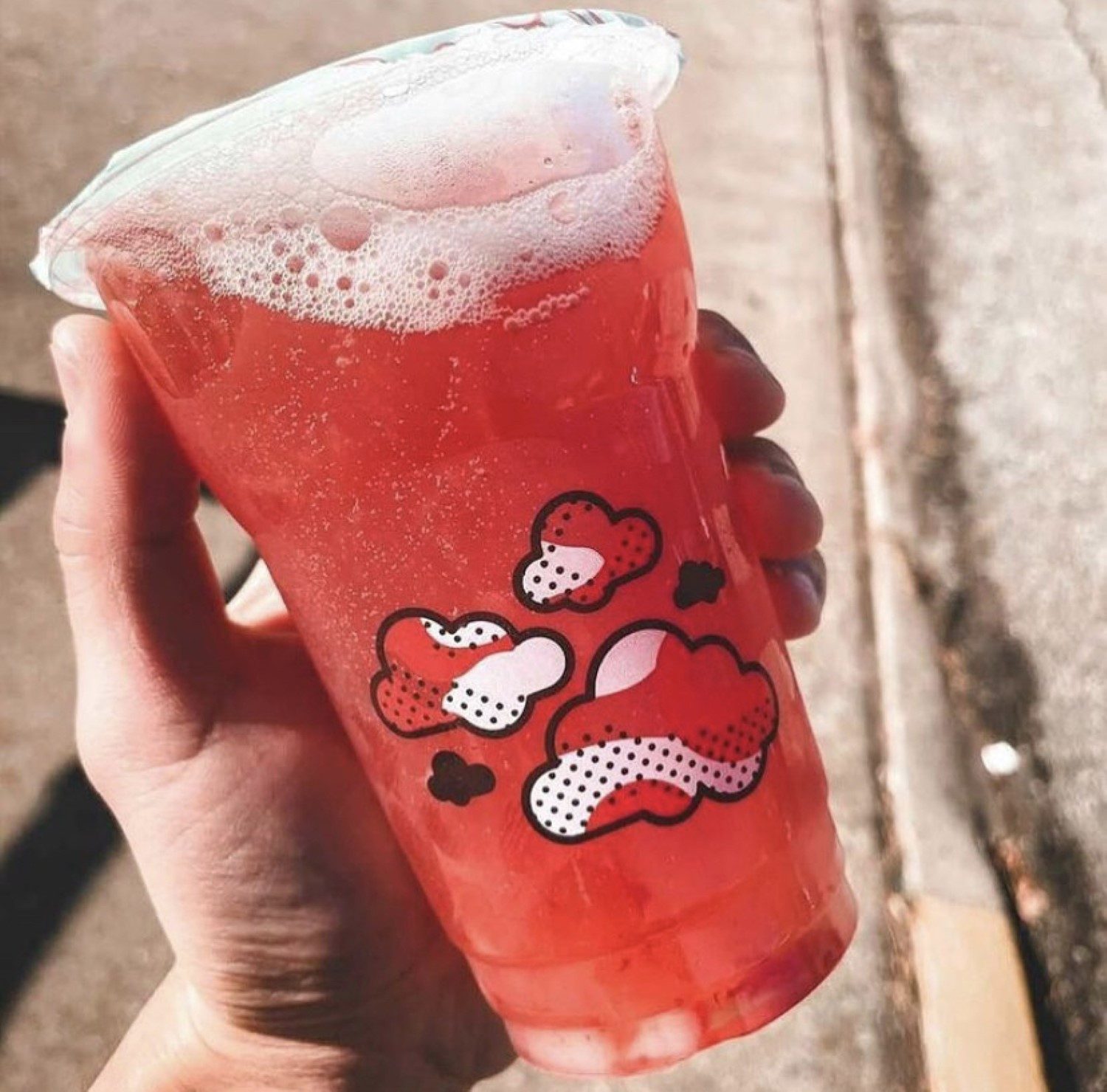 A hand holding a strawberry drink in a Kung Fu Tea cloud-logo cup