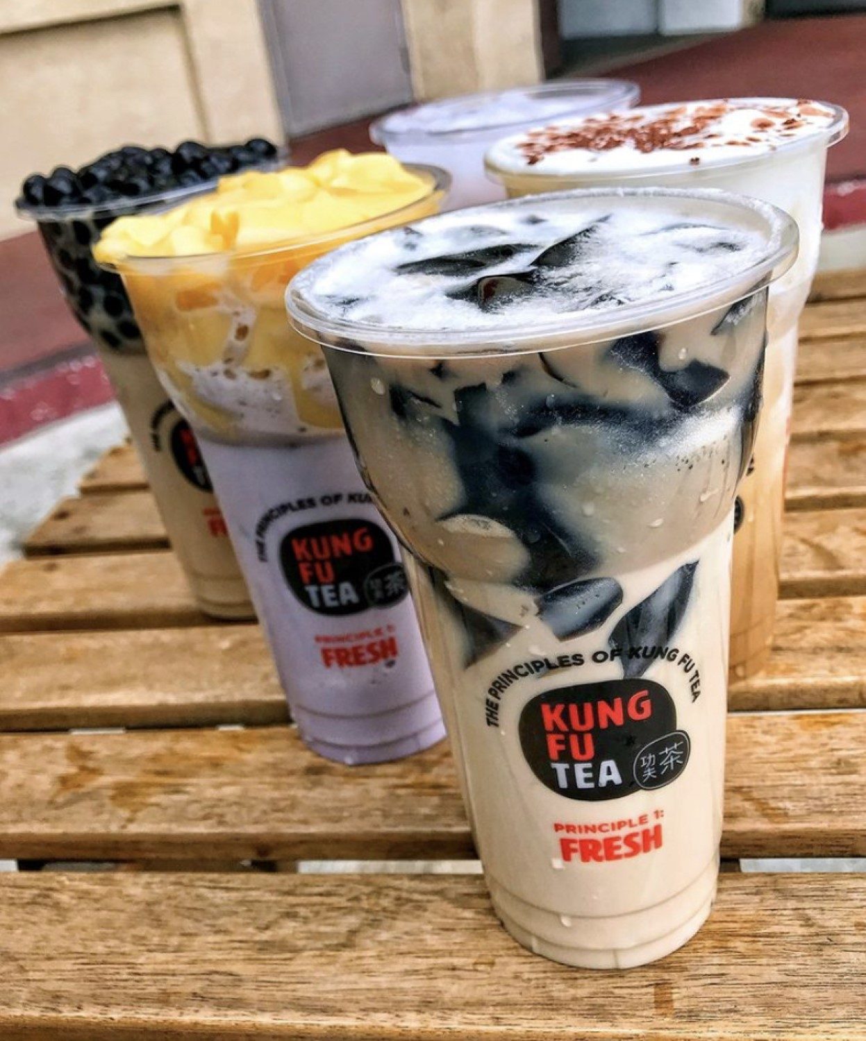 Five freshly made Kung Fu Tea drinks lined up on a wooden step, including black milk tea